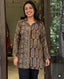 Woman wearing a patterned brown shirt standing in a doorway.