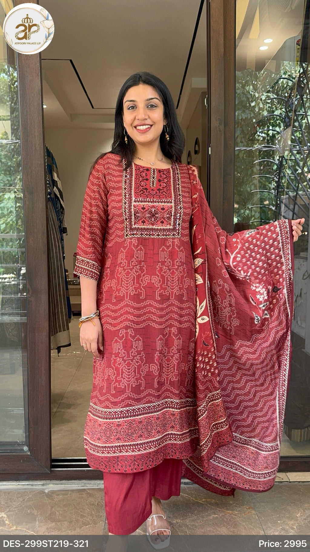 Woman wearing a traditional red and pink outfit with intricate patterns, standing indoors.