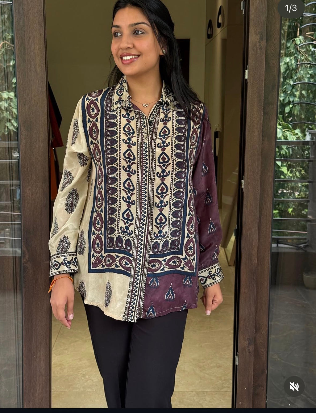 Woman wearing a patterned blouse standing in a doorway.