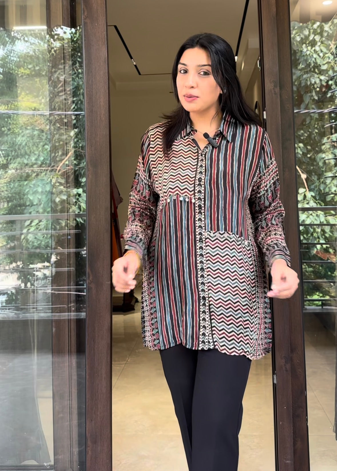 Woman wearing a patterned blouse standing in front of a glass door.