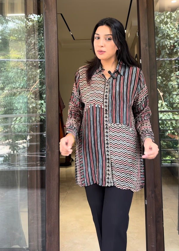 Woman wearing a patterned blouse standing in front of a glass door.