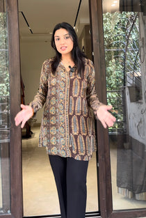 Woman wearing a patterned shirt and black pants standing in front of a glass door.