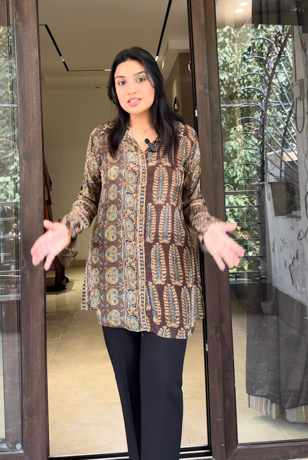Woman wearing a patterned shirt and black pants standing in front of a glass door.