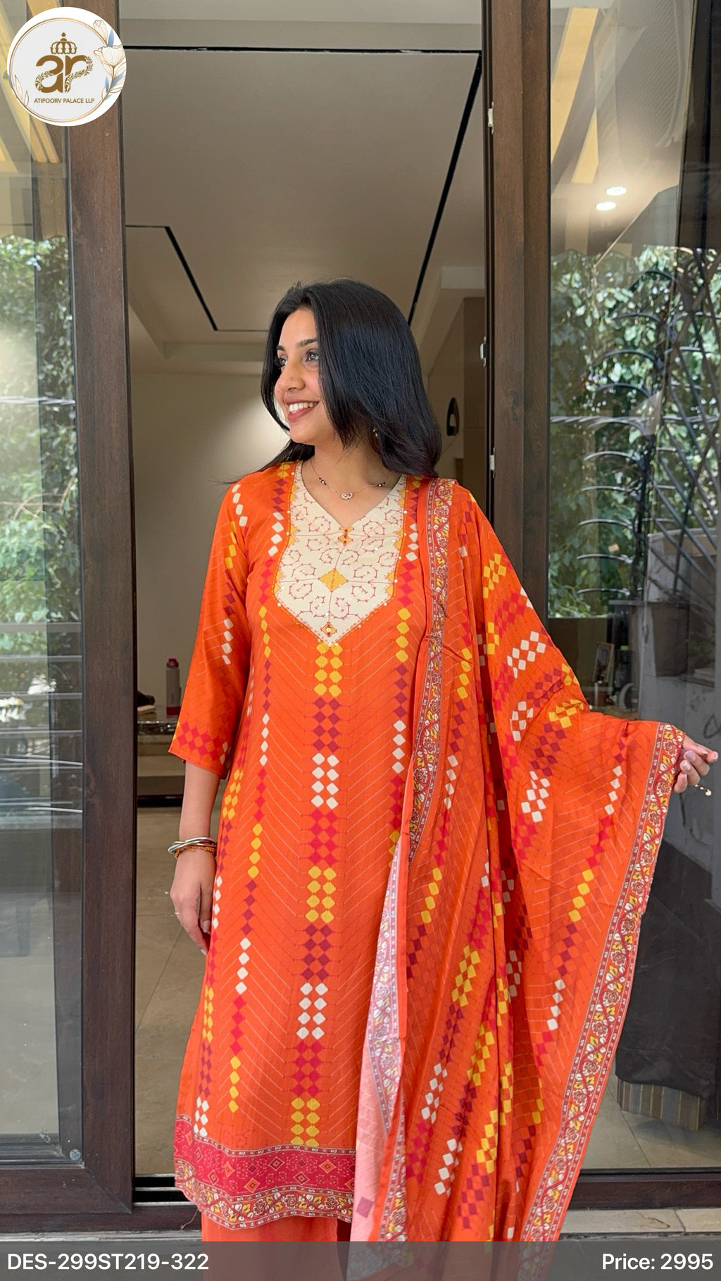 Woman wearing an orange traditional outfit with intricate patterns, standing in front of a glass door.
