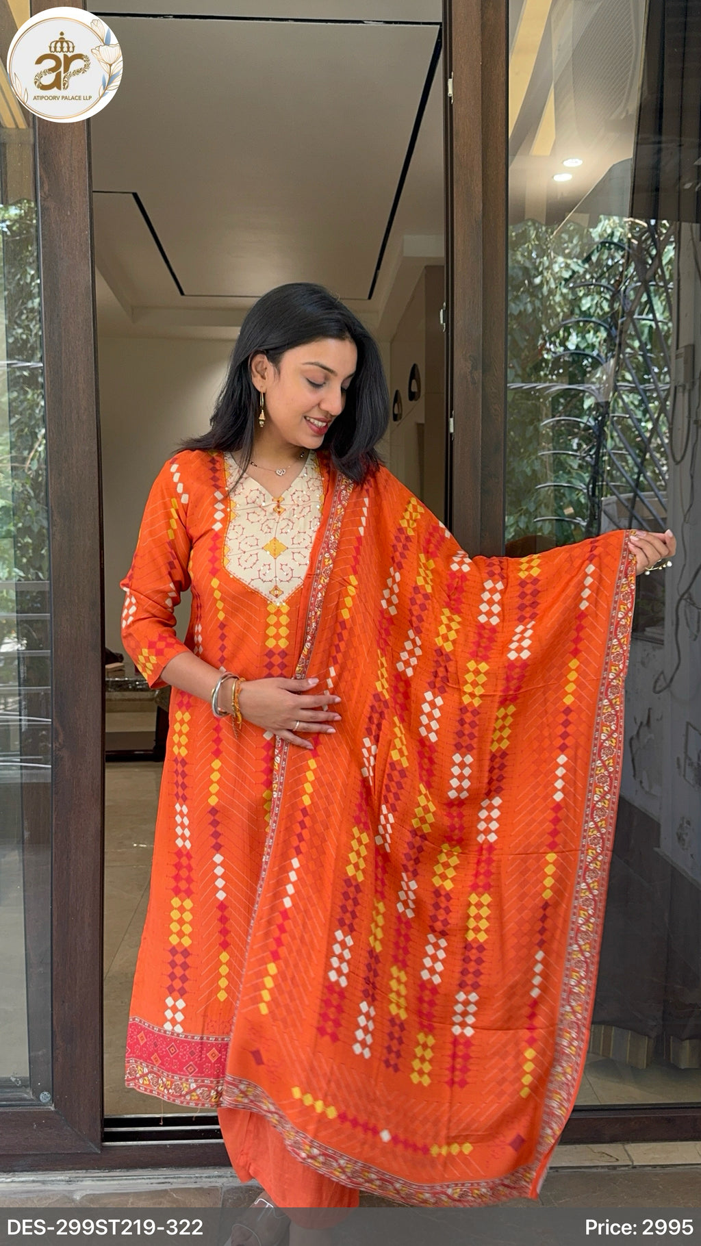 Woman holding an orange and red patterned dupatta in front of a glass door.